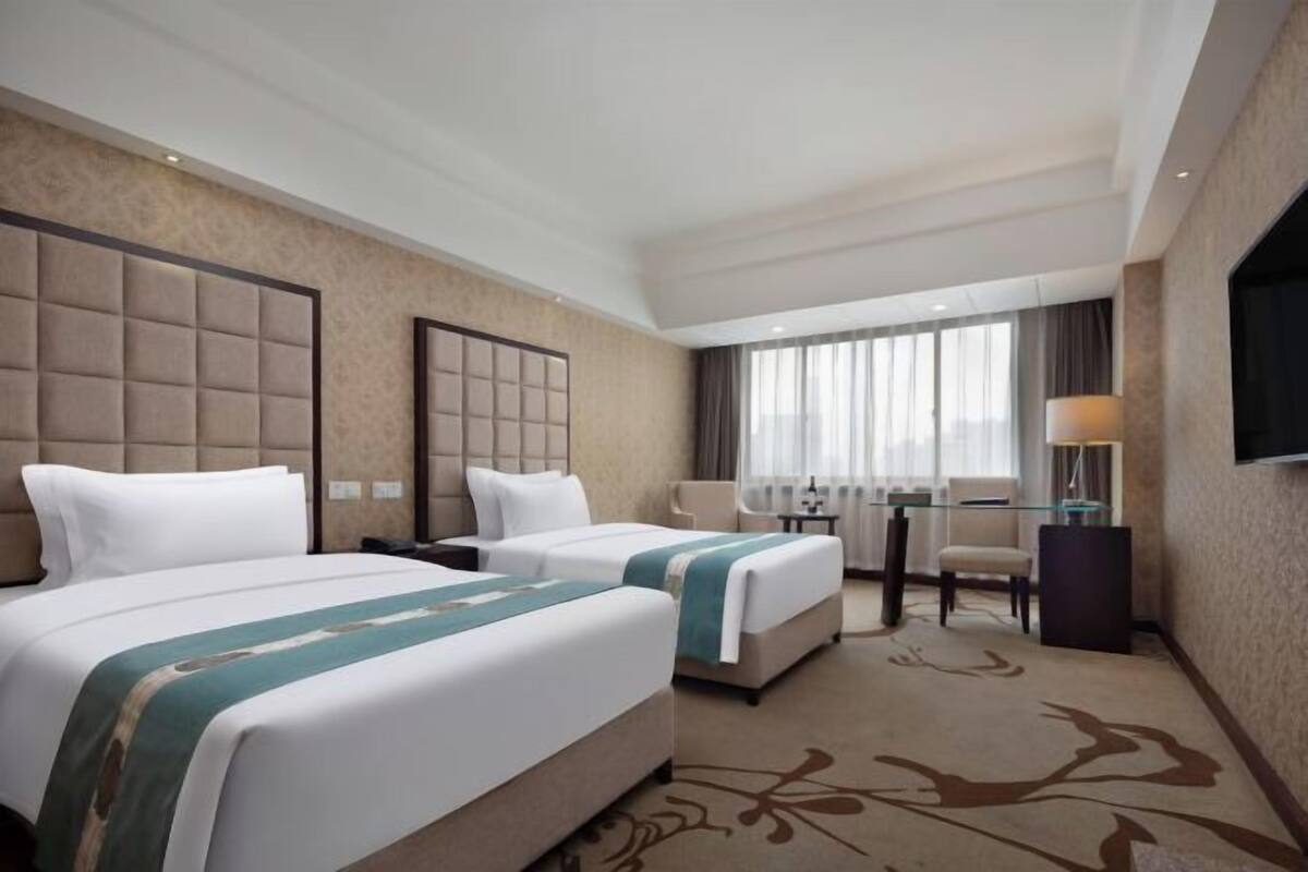 A hotel room with two beds, a desk, a chair, a television, and a large window.