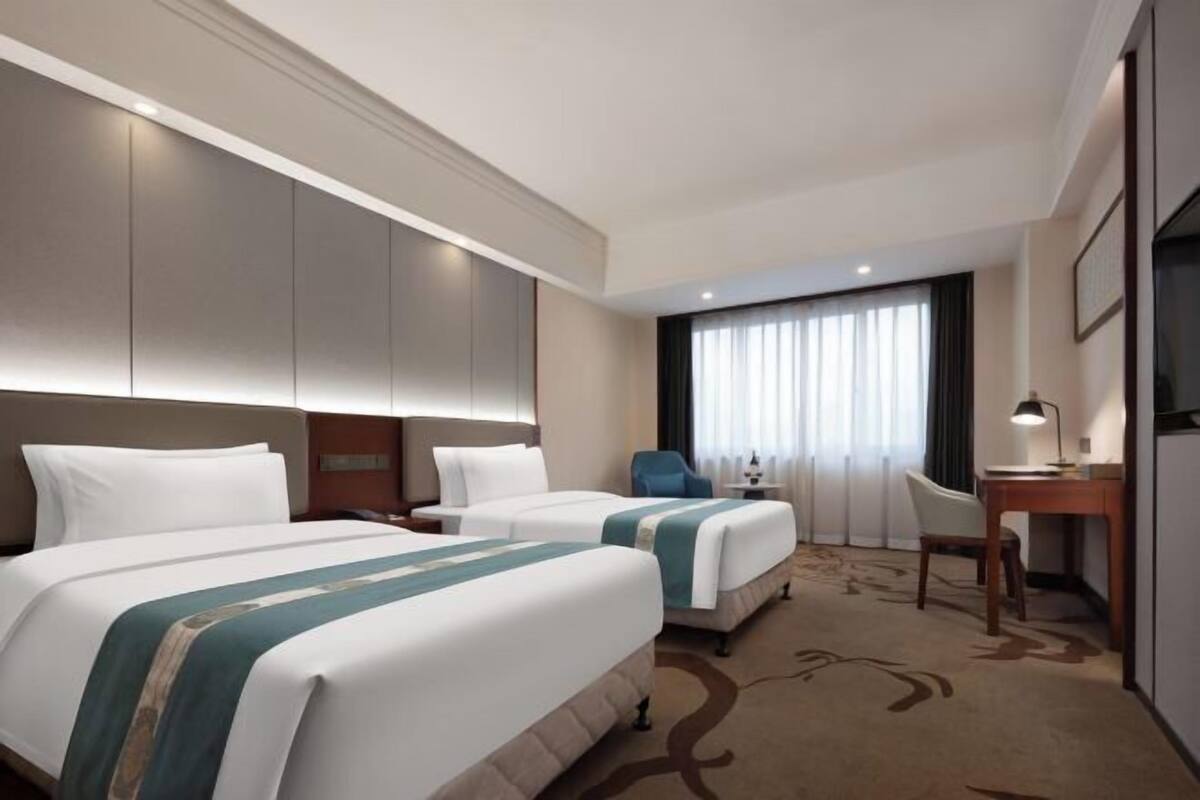 A hotel room with two beds, a desk, a chair, and a large window with curtains.