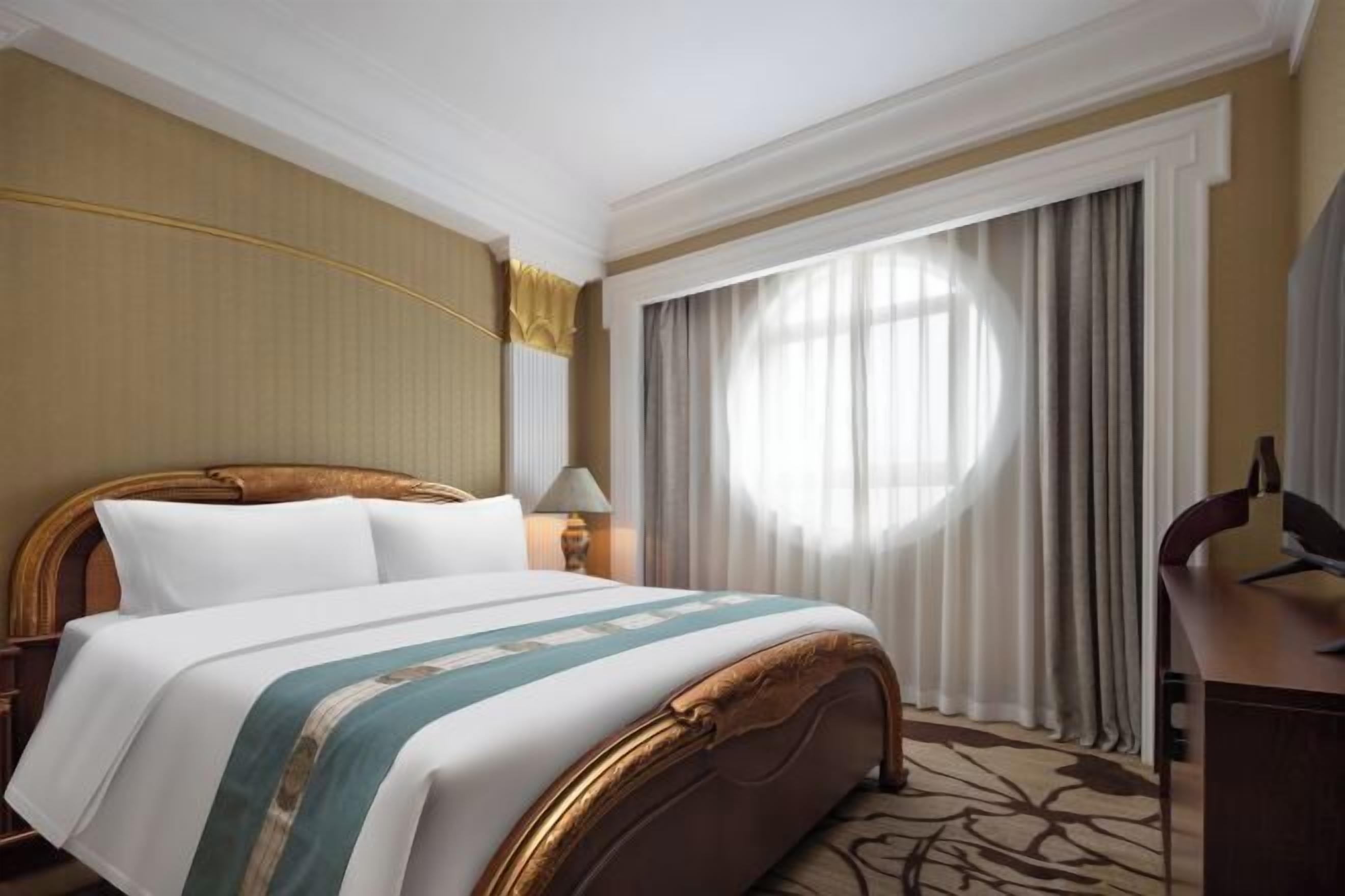 A hotel room with a bed, a desk, a lamp, and a large window with curtains.