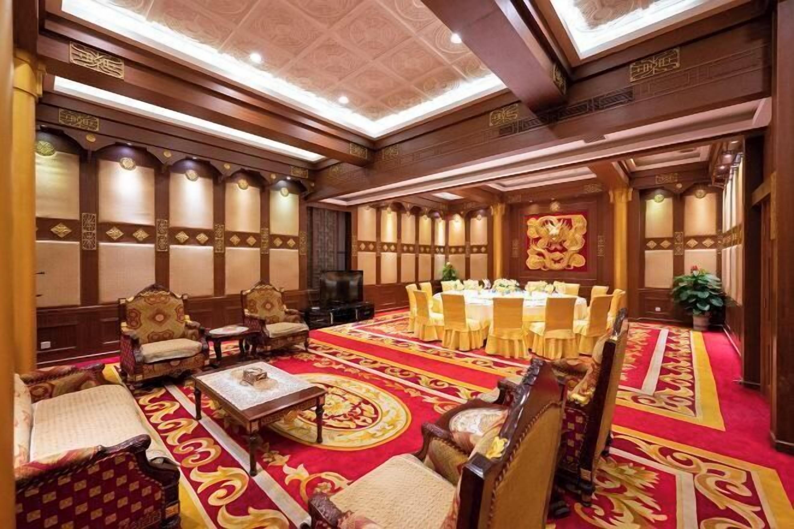 A hotel room with a large round table, multiple chairs, a sofa, and a TV.