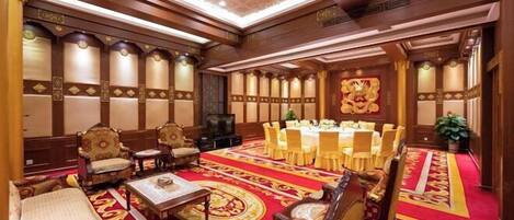 A hotel room with a large round table, multiple chairs, a sofa, and a TV.