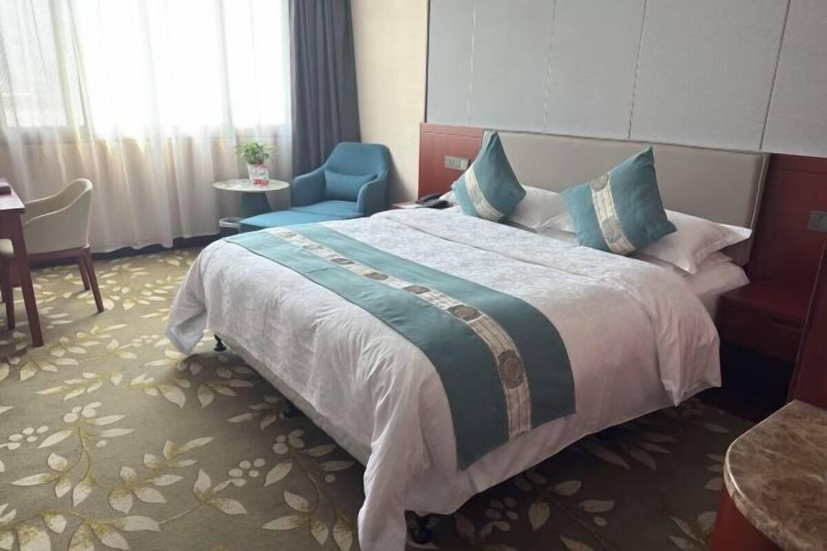 A hotel room with a bed, a chair, a small table, and a window with curtains.