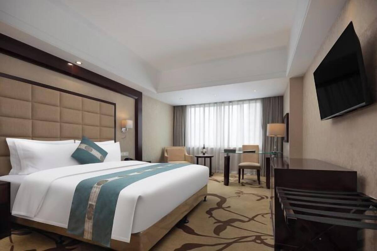 A hotel room with a large bed, a desk, a chair, a TV, and a window with curtains.