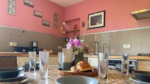A kitchen with a tiled backsplash, a dining table set with plates, glasses, and cutlery, and a vase with flowers on the table. - Le Pigeonnier du Bordial (Molières)