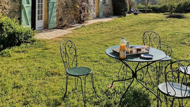 A stone building with green shutters, a grassy yard, and a table with chairs. - Le Pigeonnier du Bordial (Molières)