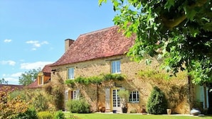 A stone house with a red roof, surrounded by a well-maintained lawn and various shrubs. - Le Pigeonnier du Bordial (Molières)