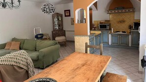 A living room with a green sofa, a wooden table, and a kitchen area with blue cabinets and a tiled backsplash. - Vacation home in the heart of Provence (Eyragues)