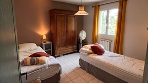 A small, cozy bedroom with two single beds, a wooden wardrobe, a bedside table with a lamp, and a window with curtains. - Vacation home in the heart of Provence (Eyragues)