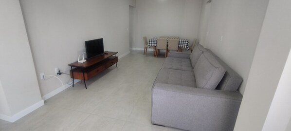 Ein Wohnzimmer mit grauem Sofa, einem Holz-Fernsehschrank und einem Esstisch mit Stühlen.