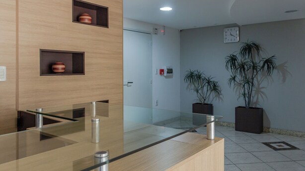 A reception area with a glass counter, wooden paneling, a clock, and potted plants. - Cozy 2 Bedroom Apartment in the center of Camboriú, 200 meters from the beach (Centro Balneário Camboriú)