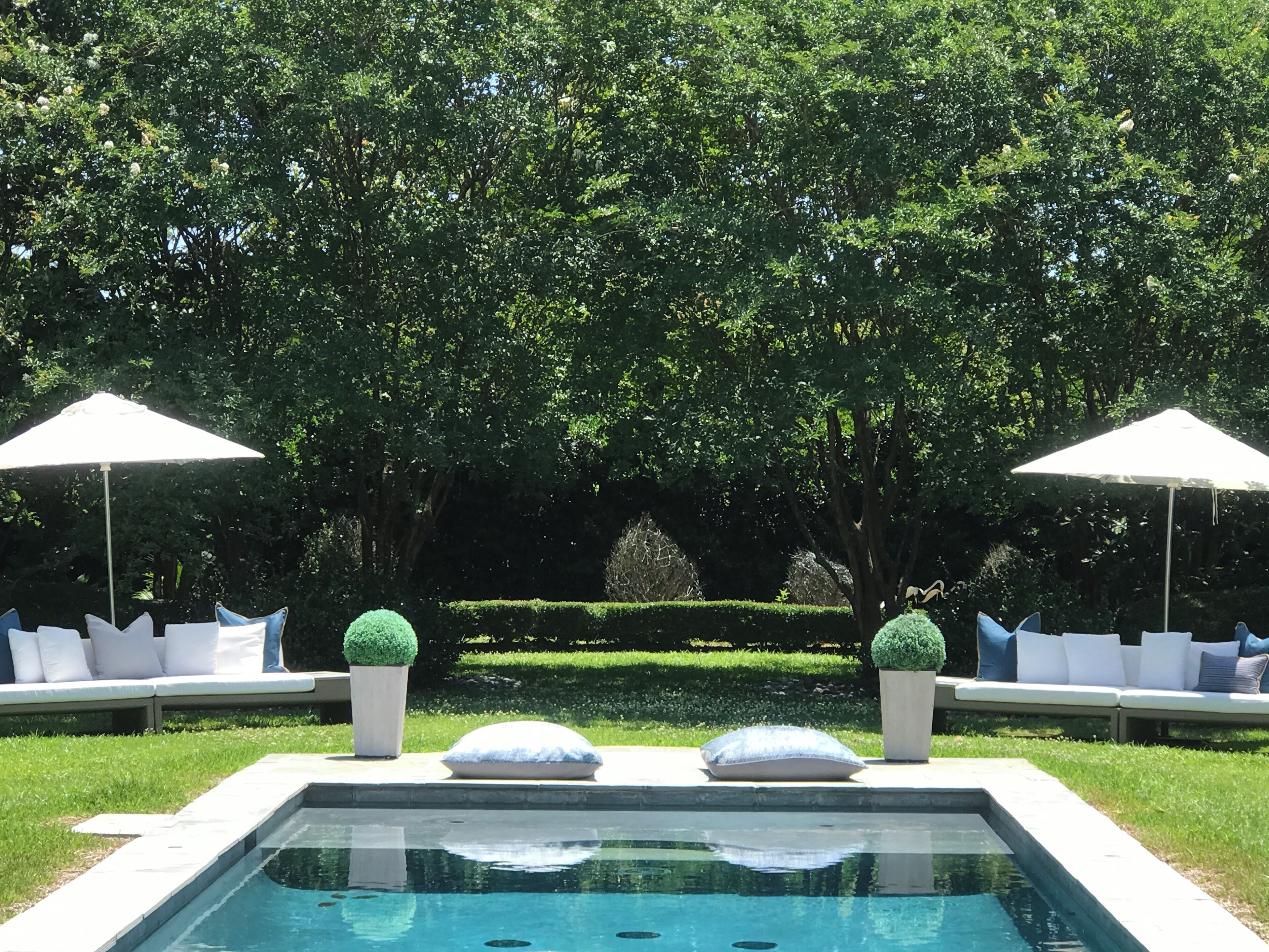 A pool with a clear view of the surrounding garden, including neatly trimmed hedges and a seating area with cushions.