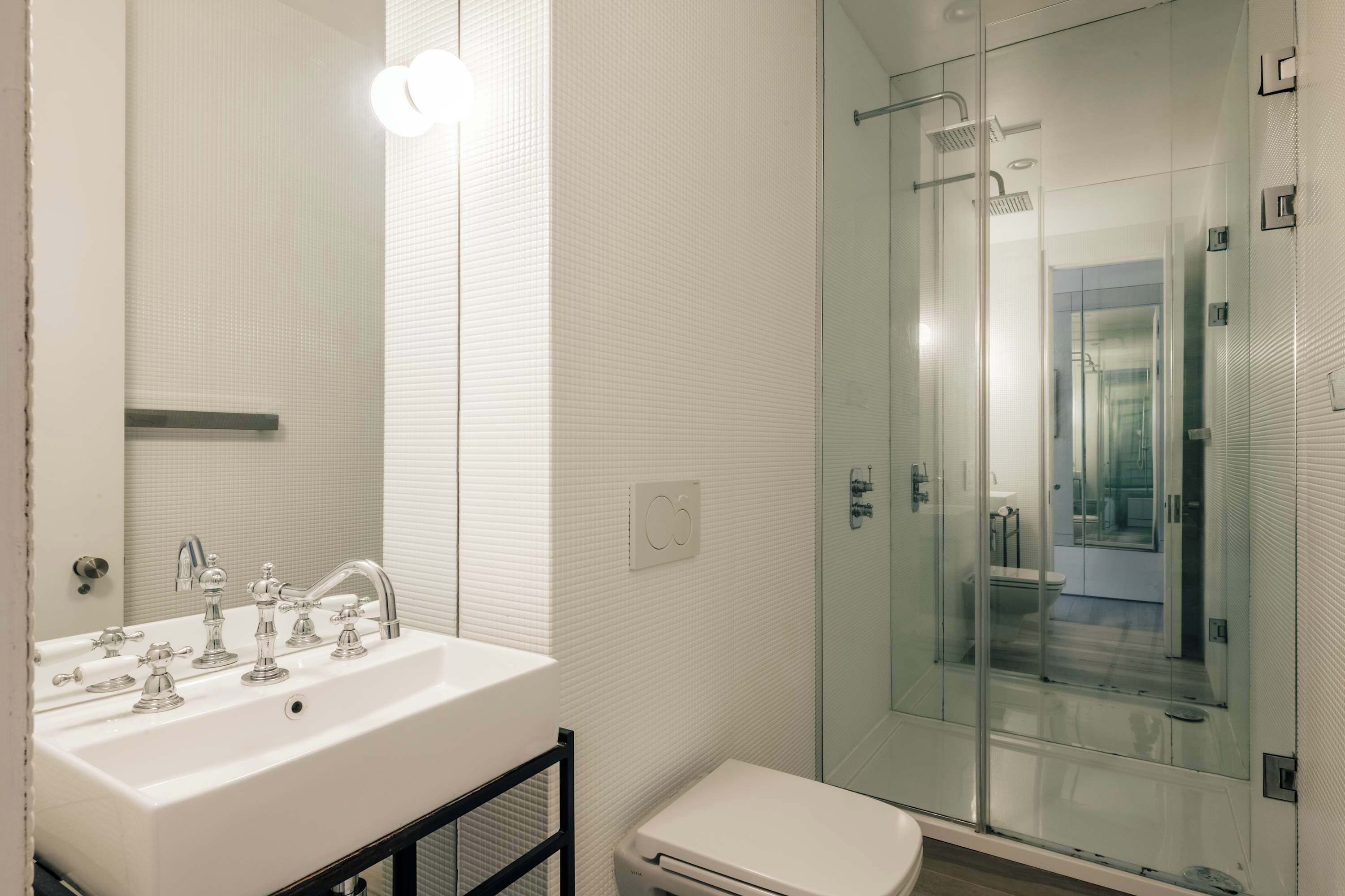 A modern bathroom with a white sink, a glass shower enclosure, and a toilet.