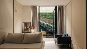 A bedroom with a bed, a chair, a small table with a vase, and a view of a garden through a glass door. - The Westlight: Bright LG Studio in White City (London)