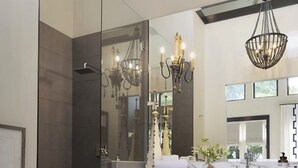 Un baño moderno con cabina de ducha, un espejo grande y una araña.