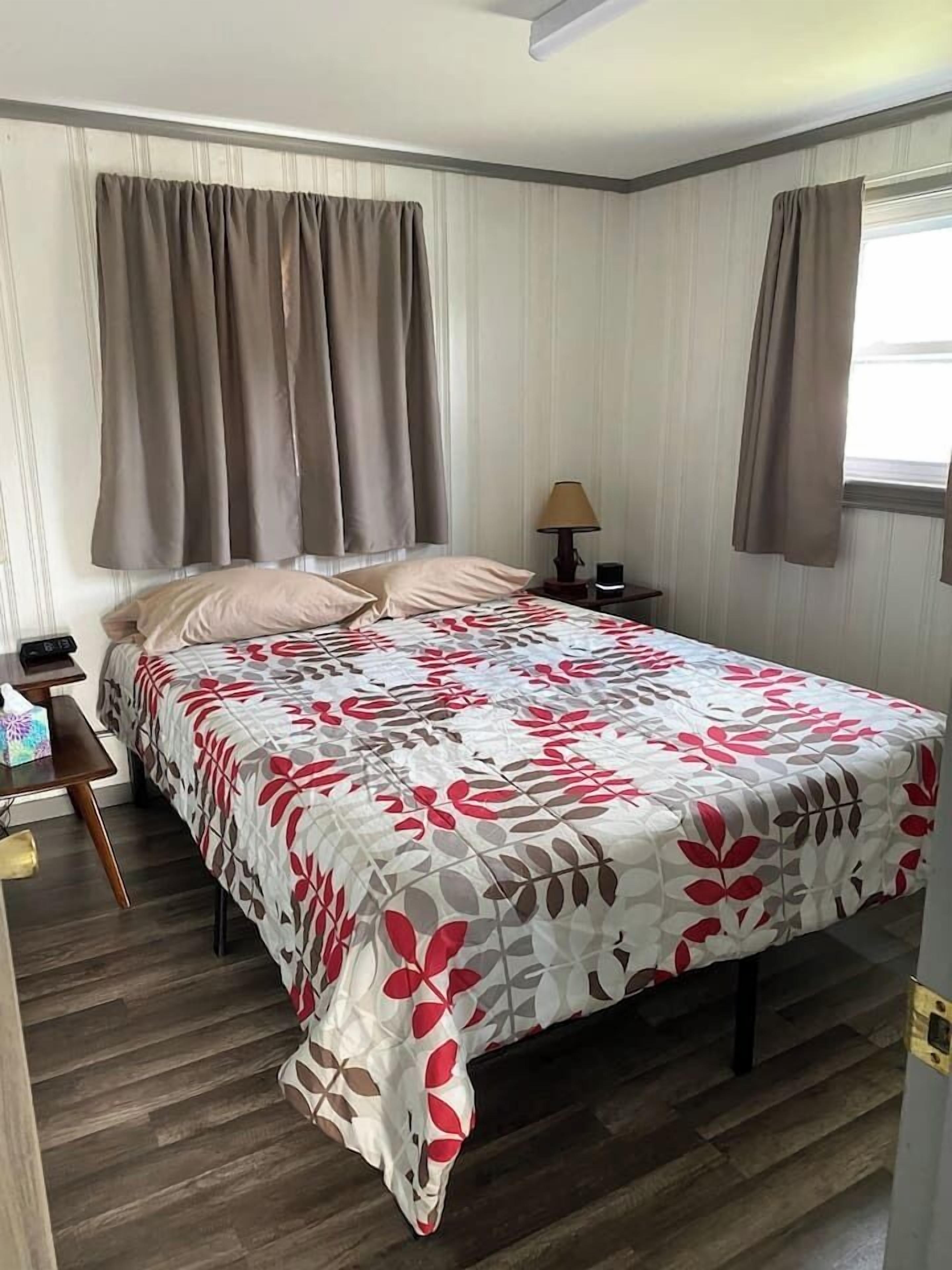 A neatly made bed with a floral bedspread, a bedside table with a lamp, and a window with curtains.