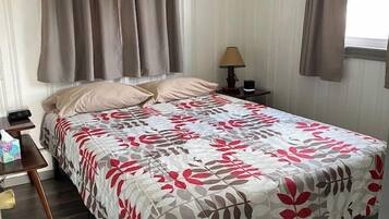 A neatly made bed with a floral bedspread, a bedside table with a lamp, and a window with curtains.