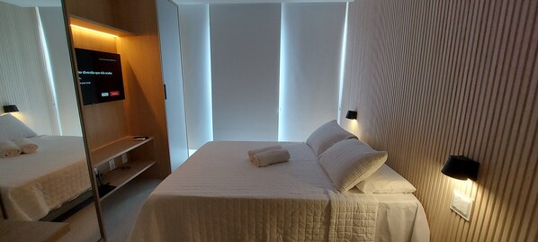 A hotel room with a bed, a TV, and a wall-mounted light fixture. - COBAR0114 - Edifício Barra Premium (Salvador)