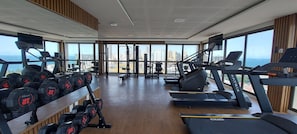 Une salle de sport équipée de tapis de course, d’haltères et d’appareils de musculation, avec de grandes fenêtres offrant une vue sur la ville.