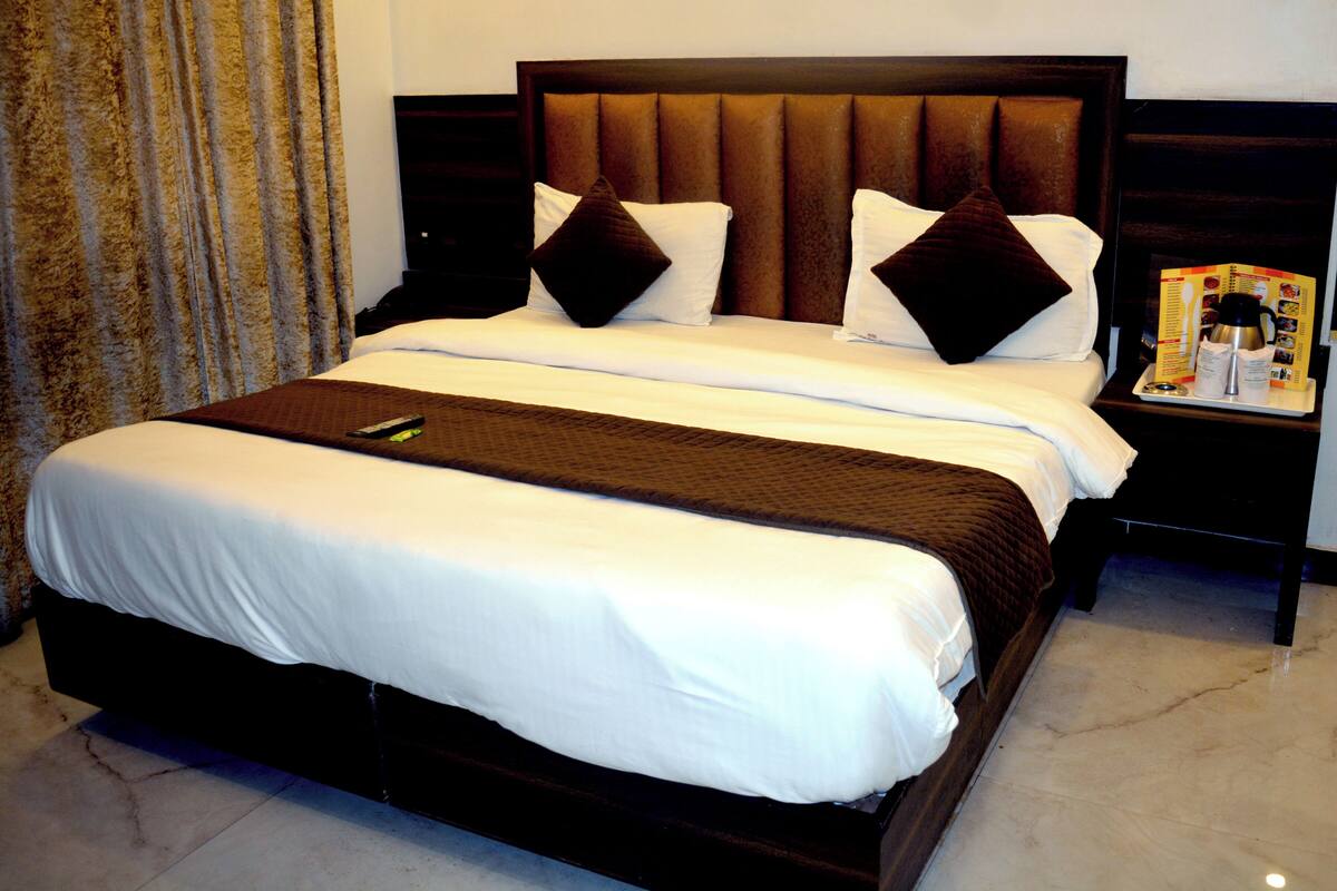 Habitación de hotel con una cama grande, cabecera de madera y una mesita de noche con cafetera y carta.