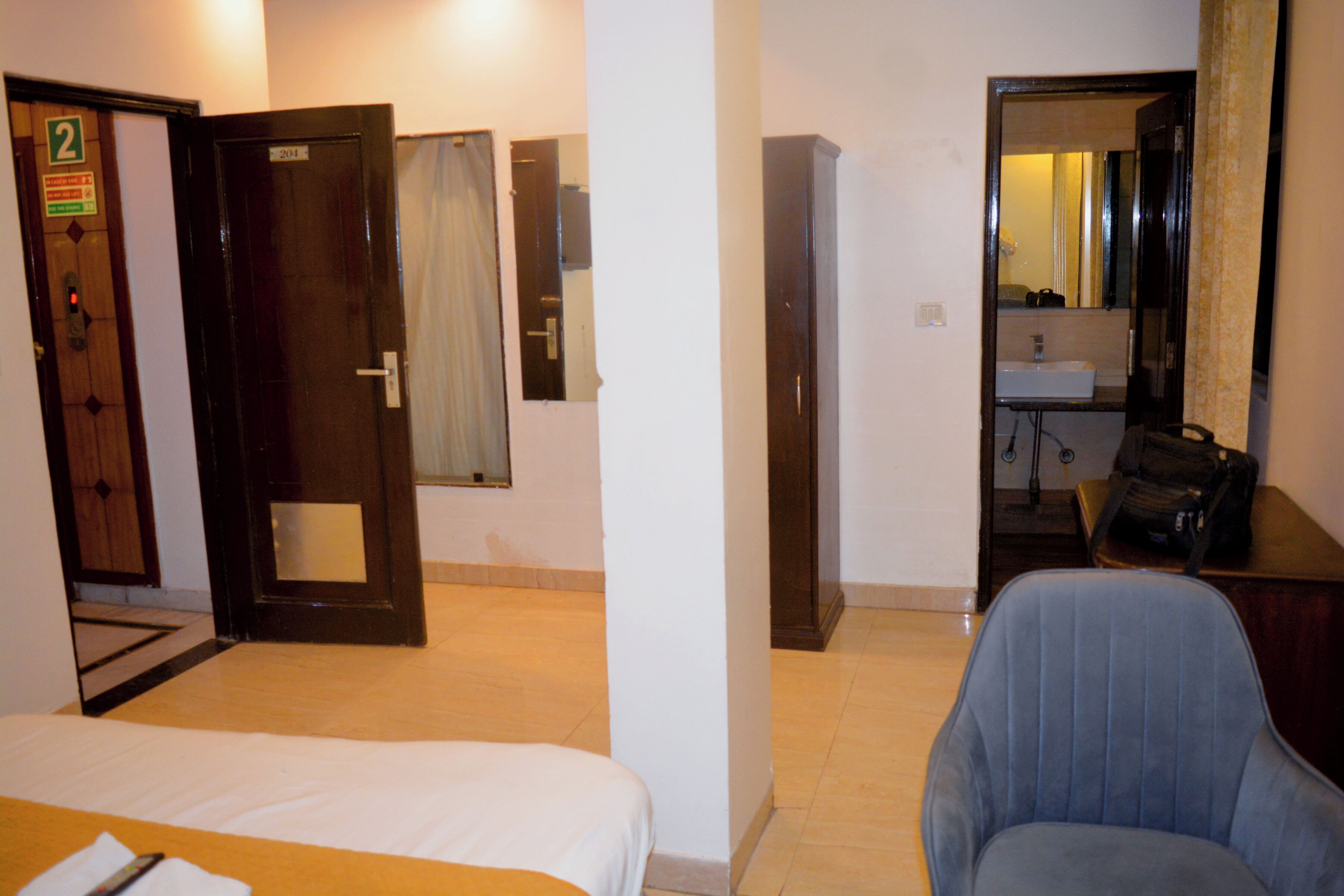 Une chambre d’hôtel avec un lit, une chaise, un bureau, un miroir et une salle de bain visible à travers une porte ouverte.