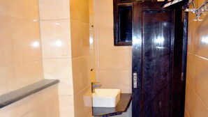 Un baño estrecho con piso de madera, inodoro blanco, lavamanos y puerta oscura.