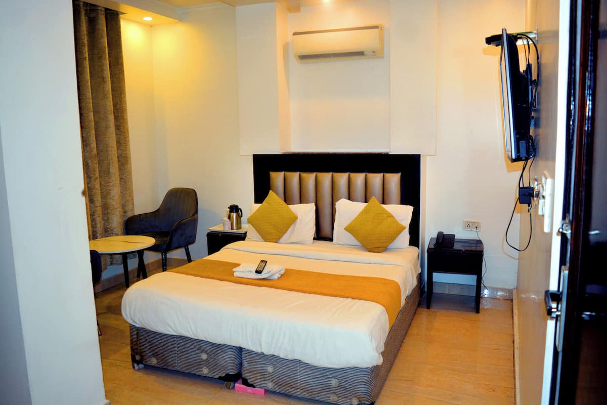 Habitación de hotel con una cama grande, una mesita de noche, una silla, una pequeña mesa, un equipo de aire acondicionado y una televisión.