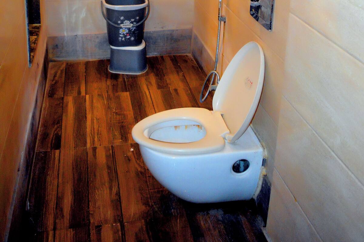 Un baño pequeño con suelo de madera, un inodoro blanco, un bidé y un estante sobre el inodoro.