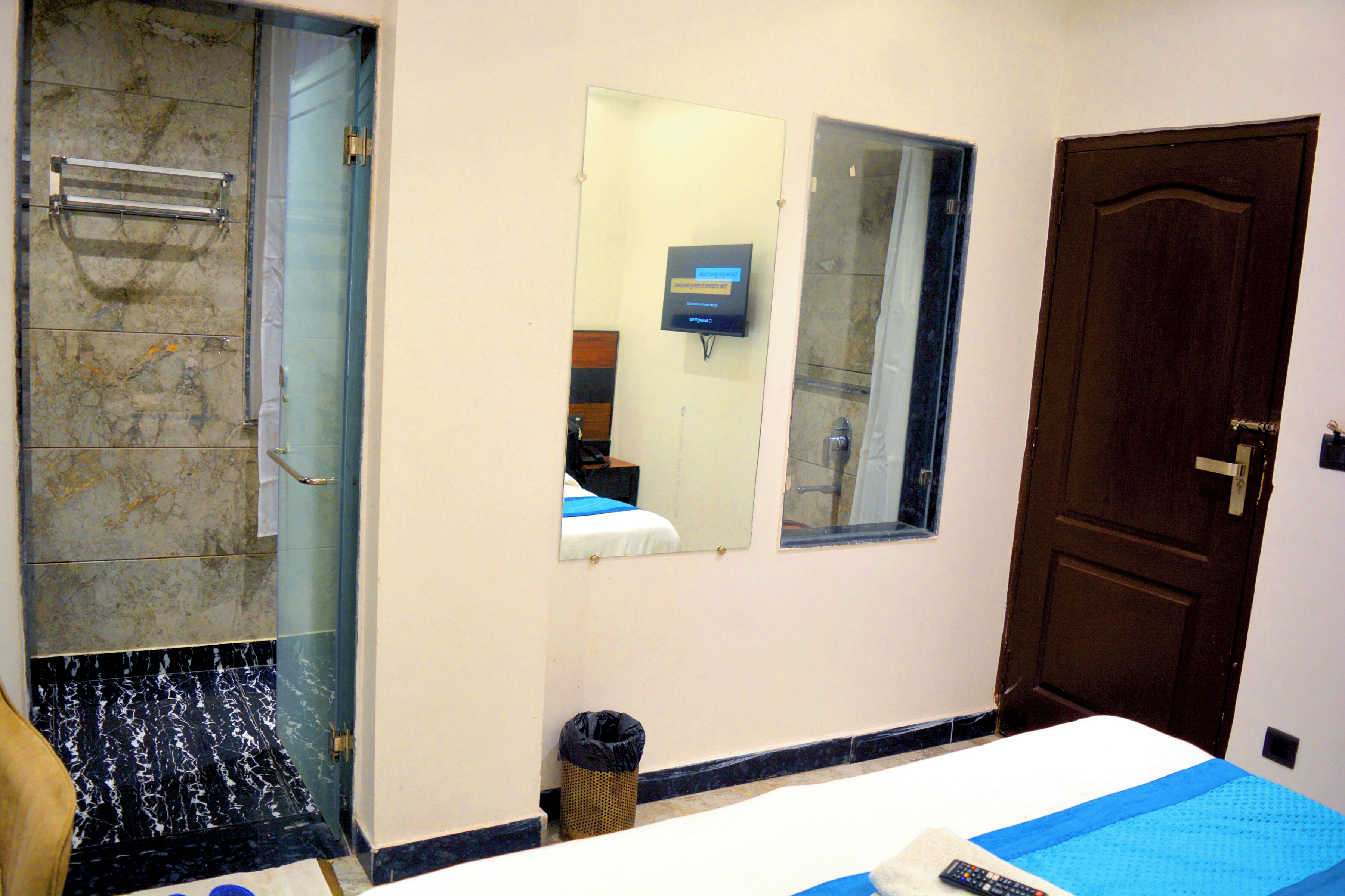 A hotel room with a bed, a bathroom with a shower, a mirror, and a door.