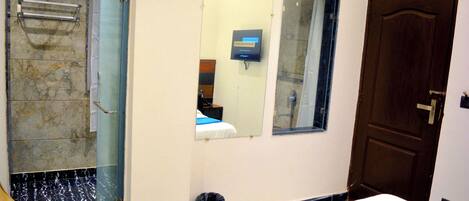 A hotel room with a bed, a bathroom with a shower, a mirror, and a door.
