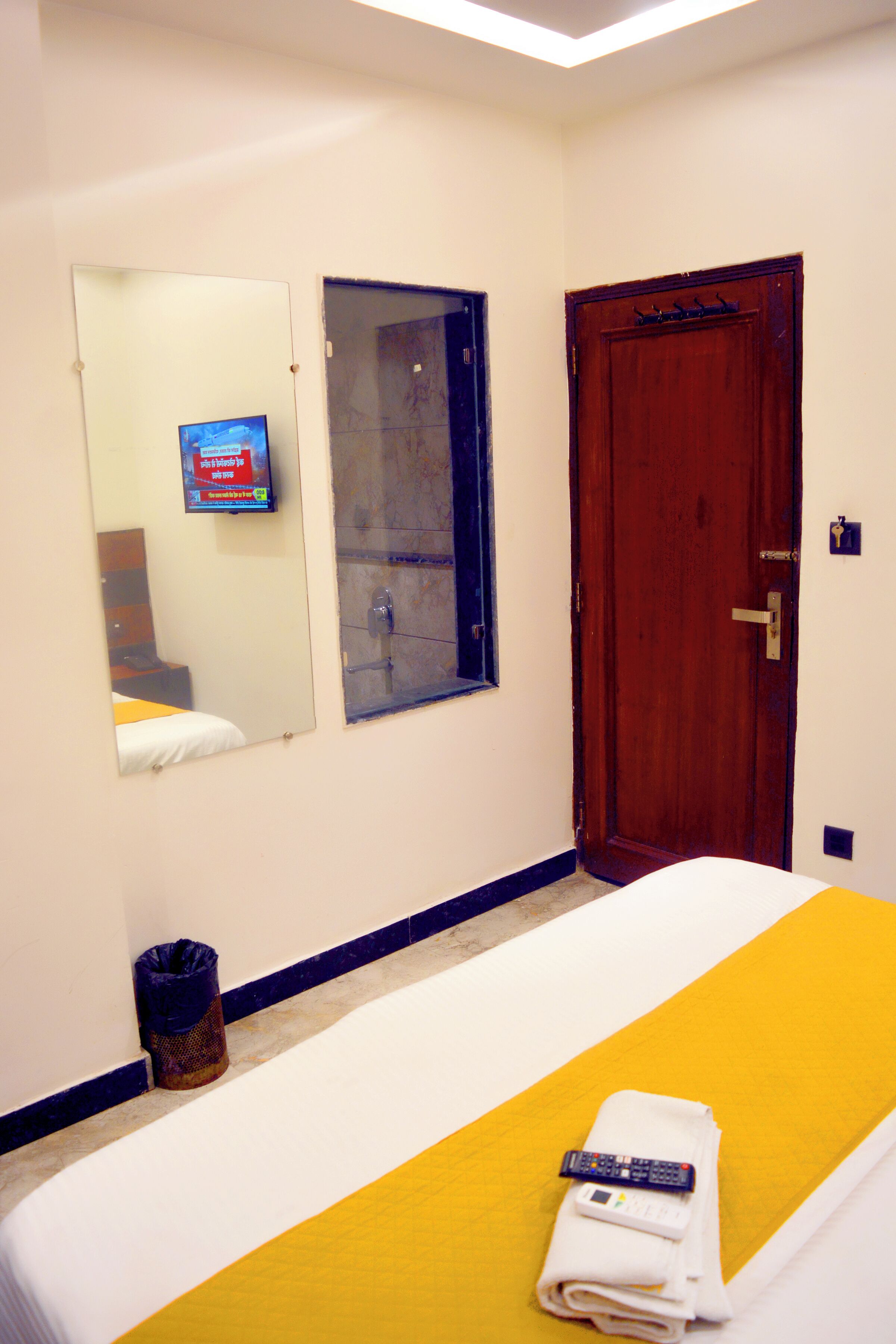 Une chambre d’hôtel avec un lit, une porte en bois, un miroir et un téléviseur fixé au mur.