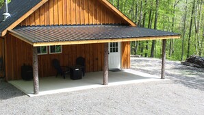 Una cabaña de madera con un porche cubierto, dos sillas y una mesa.
