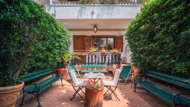 An outdoor patio with a table and chairs, surrounded by potted plants and benches. - Le Sicilien - Villa Harmony - Relax in Mondello (Palermo)