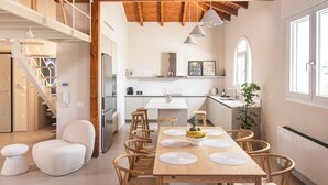 A spacious dining area with a wooden table and chairs, a white sofa, and a staircase leading to an upper level.