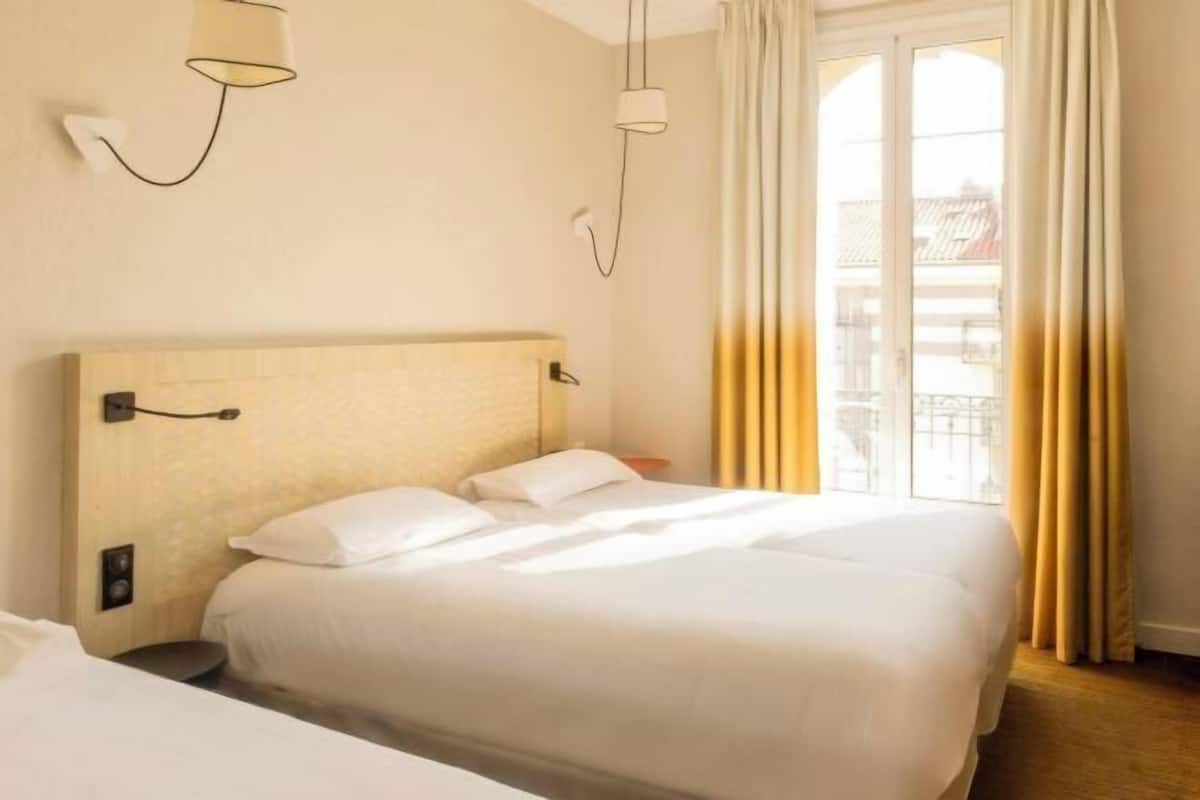 A hotel room with a large bed, a bedside table, a lamp, and a window with curtains.