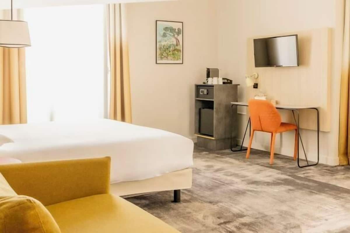 A hotel room with a bed, a desk with a chair, a television, and a painting on the wall.