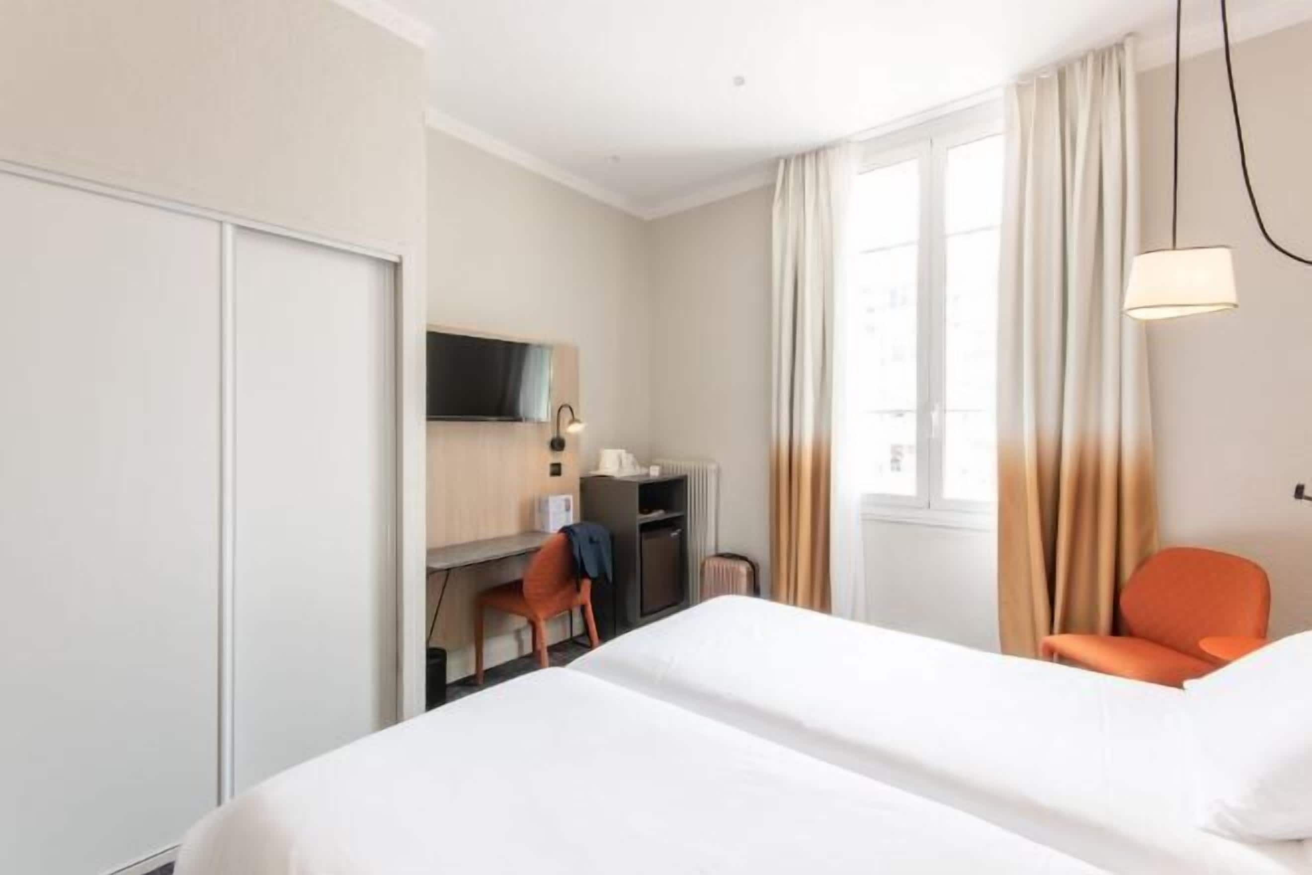 A hotel room with a bed, a desk, a chair, a TV, and a window with curtains.