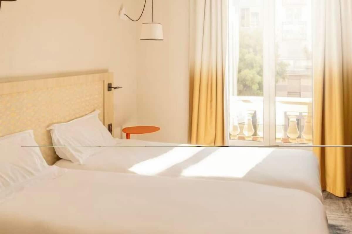 A hotel room with a large bed, a small side table, and a window with curtains.