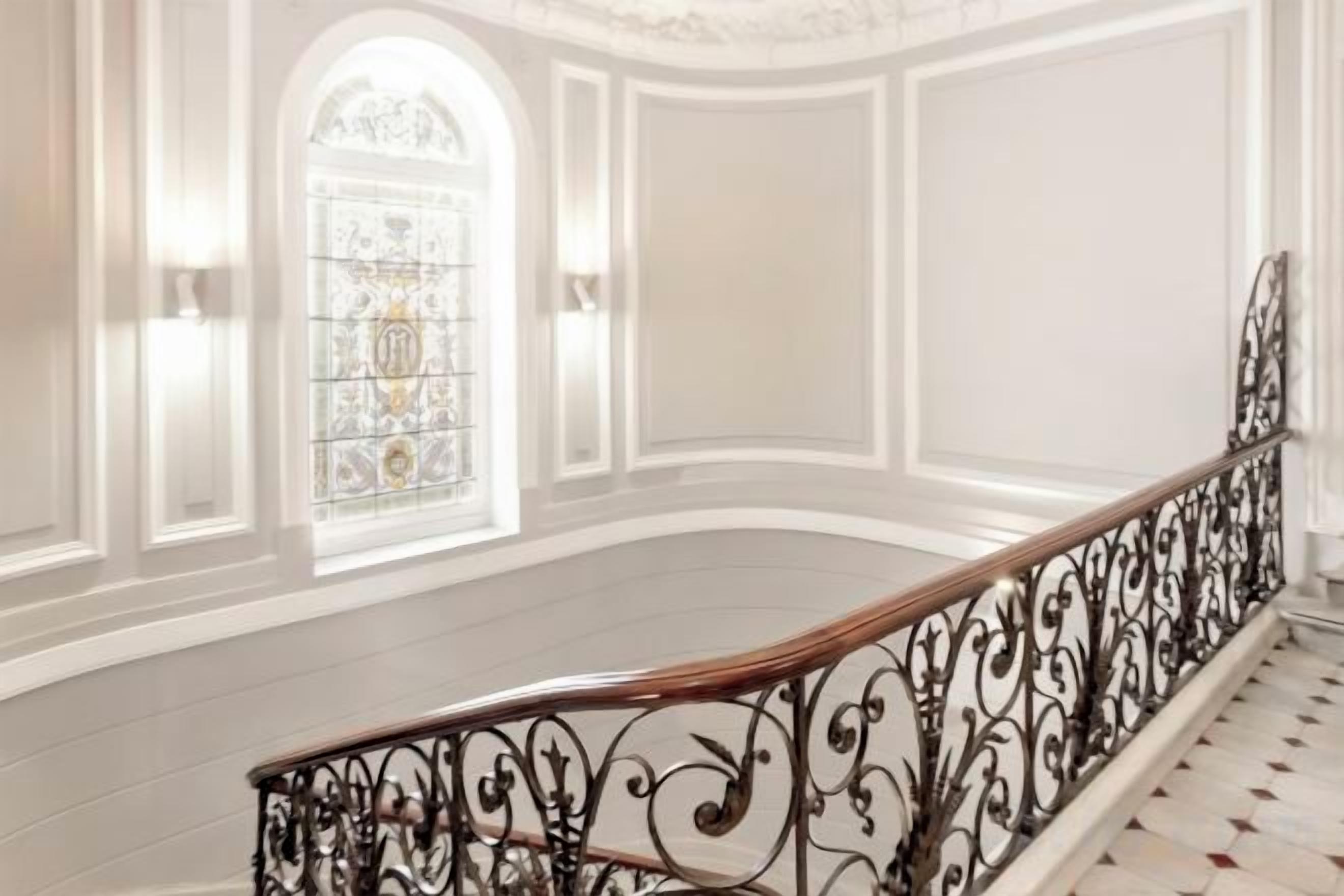 Una gran escala amb baranes metàl·liques ornamentades, interior blanc i un gran vitrall.