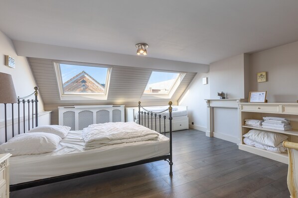 A bedroom with a skylight, a bed, a bedside table, a radiator, and a shelf with folded towels. - Holiday Home for 8 People Near the sea (Middelkerke)