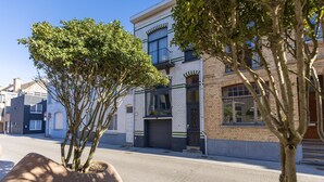 A street view with a building featuring a brick facade, a garage door, and a tree in the foreground.