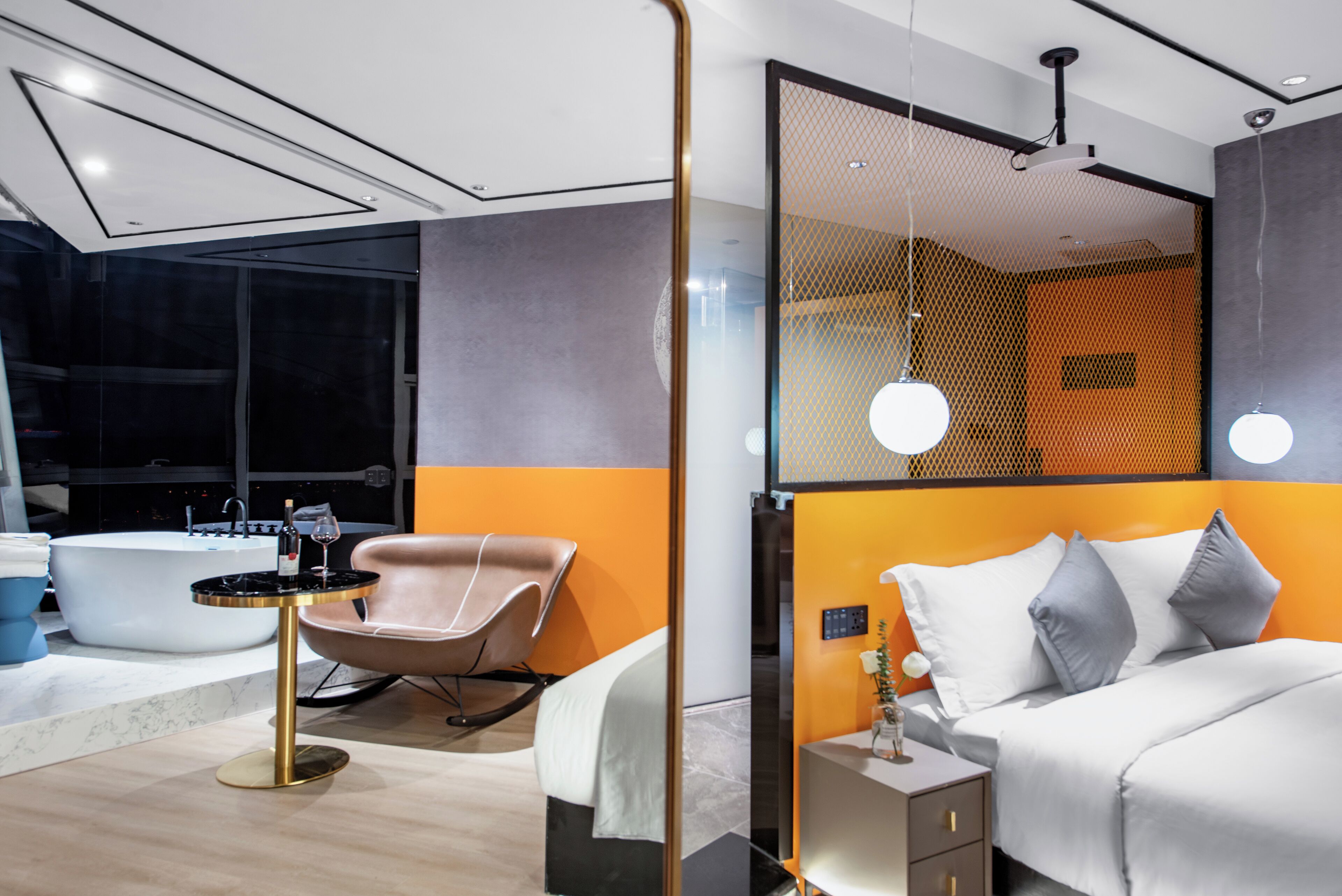 A modern bedroom with a large bed, a sitting area with a chair, a small table, and a bathtub.