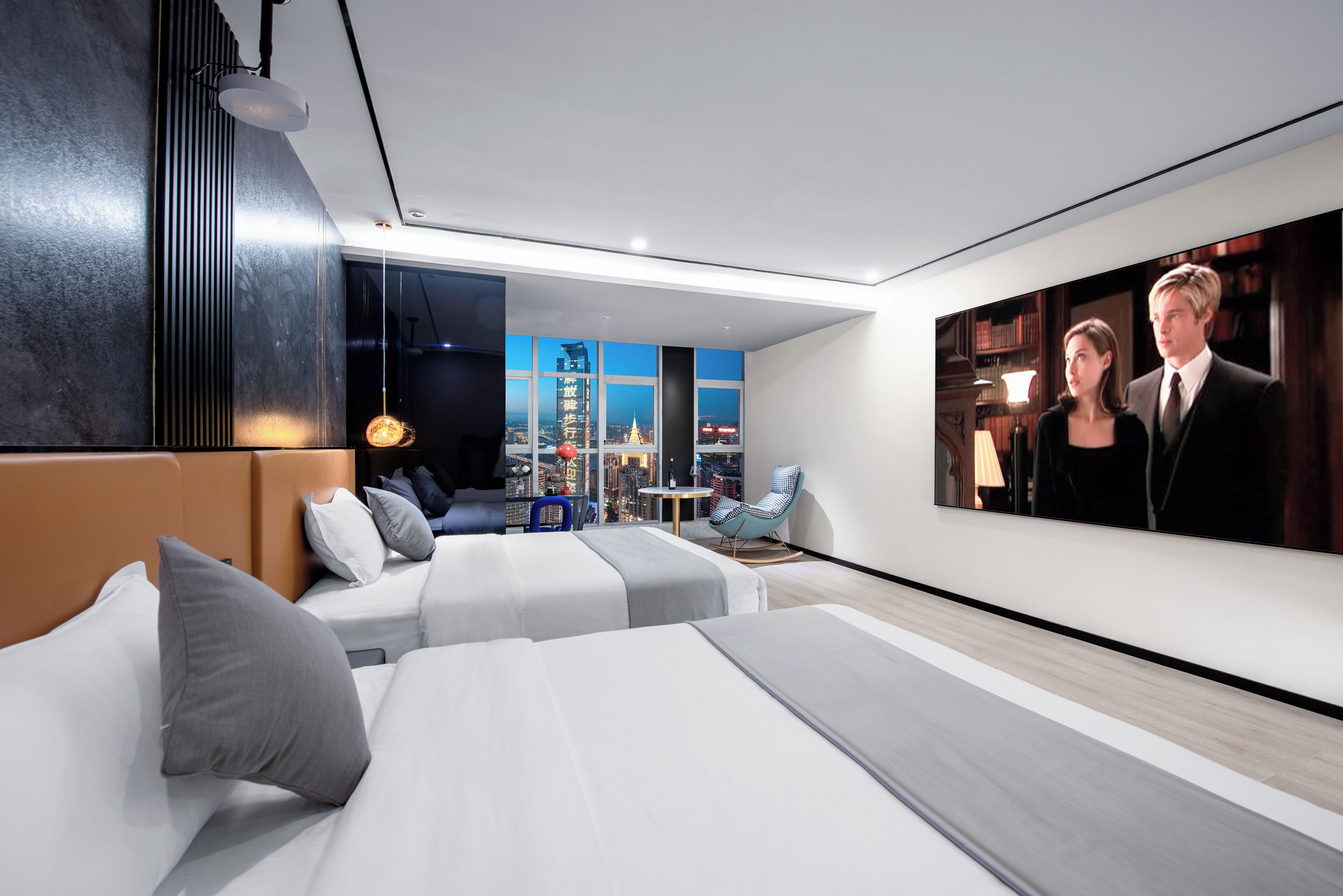 A modern hotel room with a city view, a large flat-screen TV, and a cozy seating area with a blue chair and a small table.