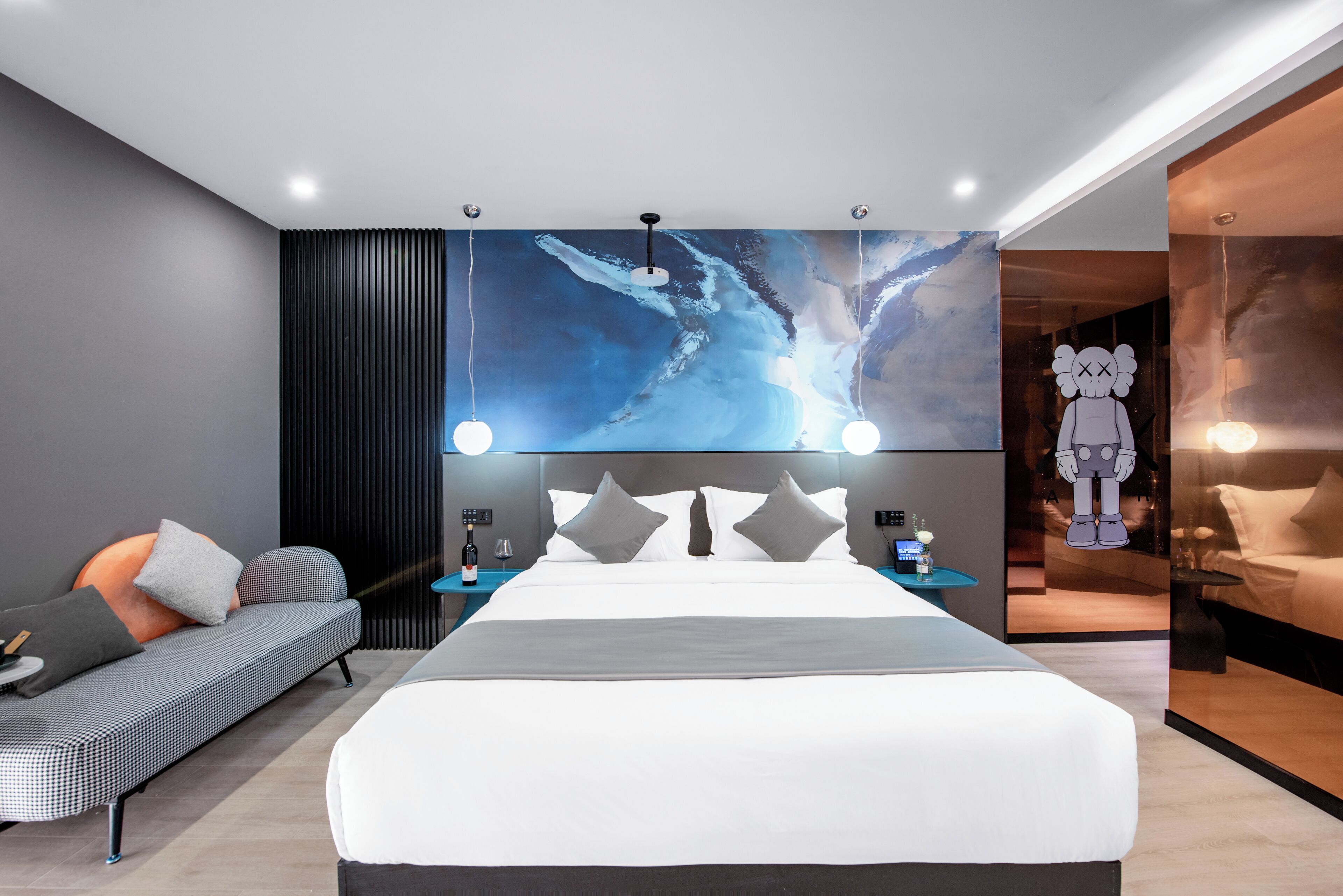 Una moderna camera d'hotel con un letto grande, una poltrona, un comodino con una lampada e un'opera d'arte appesa al muro.