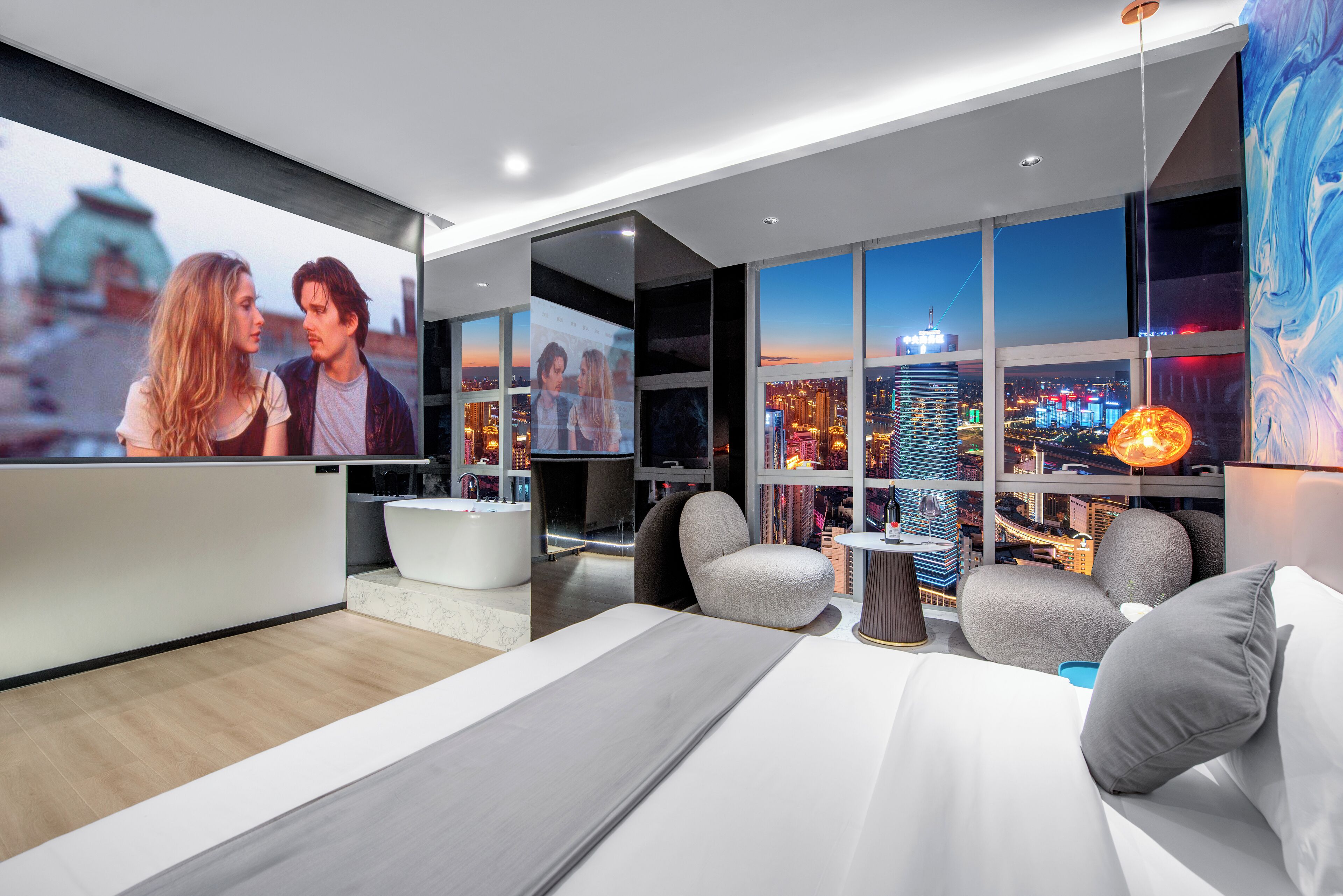 Una habitación de hotel moderna con una cama grande, un área de estar con vistas a la ciudad, una bañera y una pantalla de televisión que muestra un paisaje urbano.