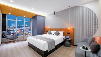 A modern hotel room with a large bed, a city view, a round table, and a cozy seating area.