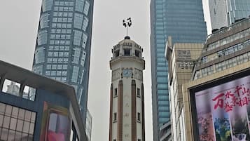 Un paysage urbain avec des gratte-ciel modernes et une tour centrale ornée d’une horloge et de quelques inscriptions.
