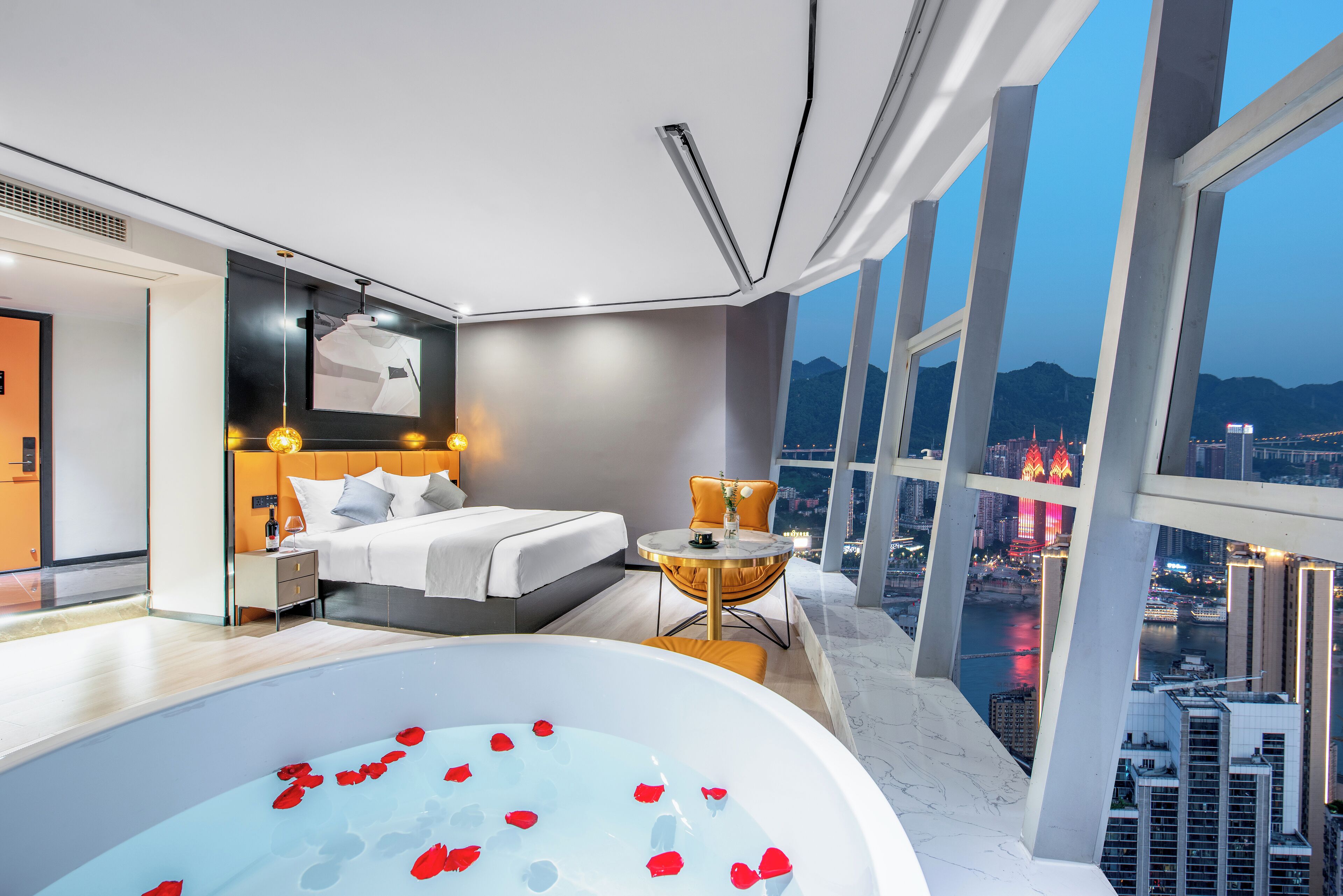 A modern hotel room with a large bed, a sitting area, and a bathtub with rose petals.