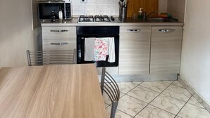 Een moderne keuken met een houten tafel en stoelen, een gasfornuis, een magnetron en een inbouwoven.