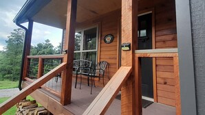 A wooden cabin with a porch, a dining area with chairs, and a window with a sign.
