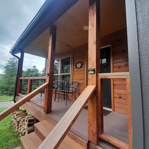 A wooden cabin with a porch, a dining area with chairs, and a window with a sign.